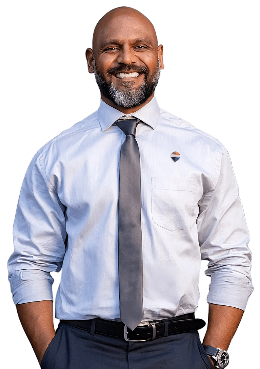 Conseiller immobilier souriant en chemise bleu clair et cravate grise, le pin REMAX épinglé sur la poche